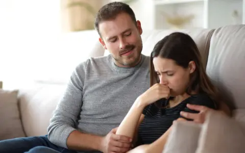 Un homme réconforte une femme en pleurs, son regard suggère une manipulation subtile, un exemple de pervers narcissique.