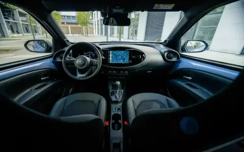 Interni moderni della Toyota Aygo X: volante, cruscotto con navigatore e sedili in tessuto.