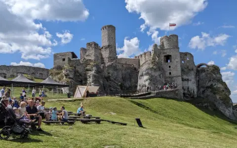 Ruiny zamku na skale, część wyżyny krakowsko-częstochowskiej, z widownią siedzącą na trawie.