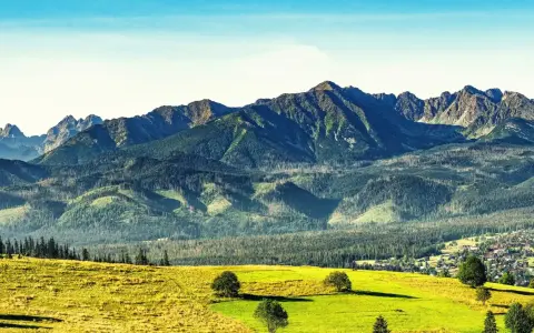 Widok na Tatry po angielsku: zielone wzgórza, lasy i skaliste szczyty. W oddali widać małą wioskę.