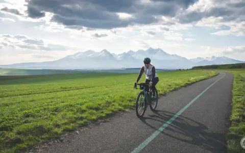 Kobieta na rowerze pokonuje malowniczą trasę z widokiem na ośnieżone Tatry. To wyzwanie: rowerem dookoła Tatr w jeden dzień!