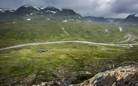 Vacker vy över fjällandskap med snöklädda toppar, en slingrande älv och stugor vid Kungsleden nära Hemavan.