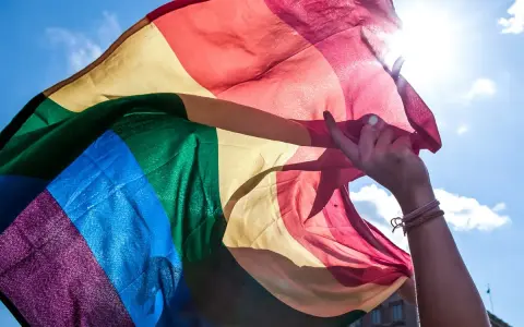 En hand håller en regnbågsflagga mot en solig himmel. En symbol för att **run for pride** och kärlek.