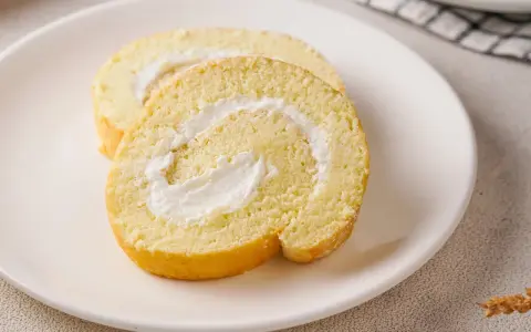 Zwei Scheiben einer leichten Biskuitrolle mit cremiger Füllung, perfekt für ein Zitronenrolle Rezept.