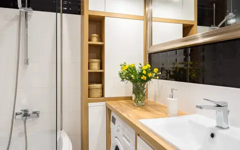 Une petite salle de bain moderne avec une douche, un lavabo, une machine à laver et des paniers en osier sur des étagères en bois.