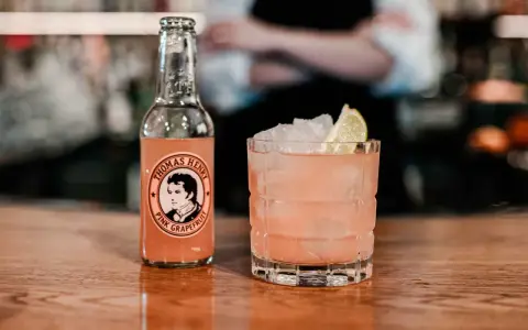 En rosa tequila drink med is och lime, bredvid en flaska Thomas Henry Pink Grapefruit.