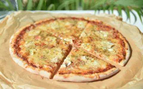 Pizza 4 sery z roztopionym serem i ziołami na papierze do pieczenia.