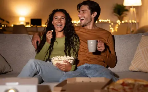 Ein lachendes Paar genießt einen gemütlichen Filmabend mit Popcorn und Pizza. Perfekte filmabend snacks für einen entspannten Abend.