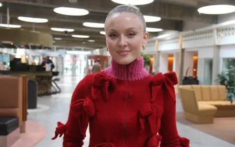 Zara Larsson i USA, klädd i en röd tröja med rosetter, ler mot kameran.