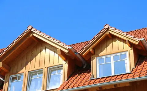 Holzverkleideter Dachausbau mit Gaube und roten Ziegeln unter blauem Himmel.