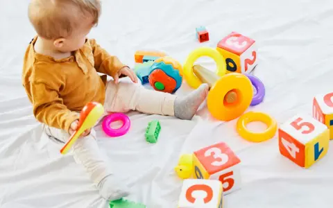 Roczne dziecko bawi się kolorowymi klockami, pierścieniami i grzechotką. Idealne gry dla rocznego dziecka.