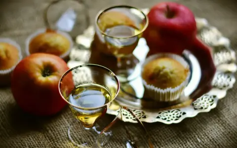 Zwei Gläser mit goldenem Schnaps, Äpfel und Muffins auf einem Silbertablett. Perfekt für den Genuss von selbstgemachtem Kartoffelschnaps.