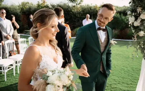 Para Młoda trzyma bukiet, a Pan Młody w zielonym garniturze uśmiecha się do niej. To piękny moment podczas urlopu okolicznościowego ślub.
