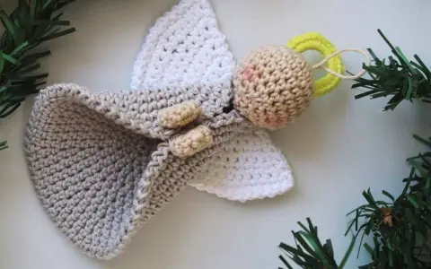 Un tierno angel amigurumi de ganchillo, con alas blancas y un cuerpo gris, adornado con ramitas verdes.