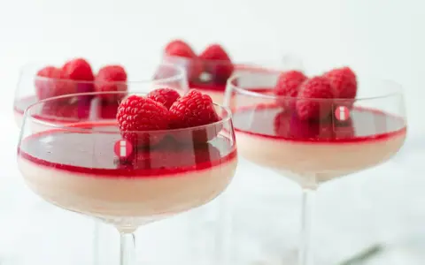 Flera glas med krämig pannacotta, toppad med hallon och en röd sås. En perfekt dessert i glas.