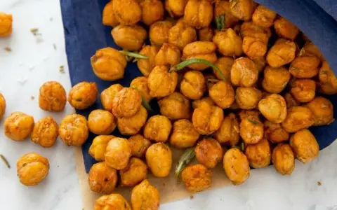 Un sacchetto blu rovesciato rivela una montagna di ceci croccanti al forno, dorati e invitanti, con qualche rametto di rosmarino sparso tra loro.