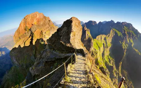 Pfad über Felsen zum Pico Ruivo, Madeira. Steile Hänge, grüne Vegetation und ein schmaler Weg mit Seilsicherung.