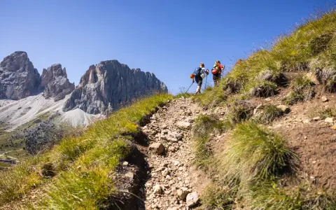 Due escursionisti affrontano un sentiero roccioso sui **cammini in Trentino**, con imponenti vette sullo sfondo.