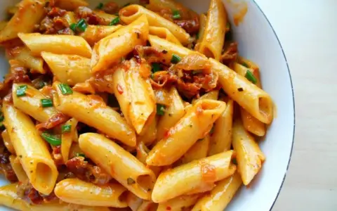 Penne z sosem z suszonych pomidorów i zieloną cebulką, danie wygląda apetycznie.