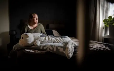 En kvinna sitter i sängen med en stor kramdjursko. Hon ser ut att fundera, kanske över sina två personligheter.