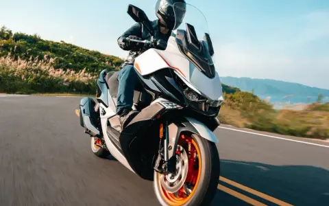 Kymco Xciting 400i dane techniczne: skuter z kierowcą na krętej drodze, z widokiem na góry i jezioro w tle.