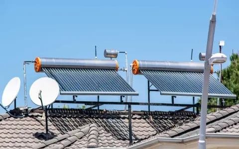 Dos calentadores de agua caliente solar en un tejado, junto a antenas parabólicas, bajo un cielo azul.