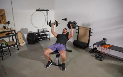 Homme faisant un exercice banc de musculation avec haltères.