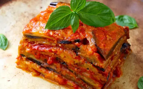 Una fetta di parmigiana di melanzane, stratificata e succulenta, guarnita con basilico fresco.