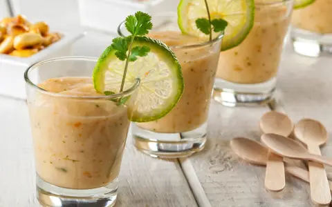 Erfrischende Gläser mit cremiger Tigermilch, garniert mit Limettenscheiben und Koriander. Kleine Holzlöffel liegen bereit.