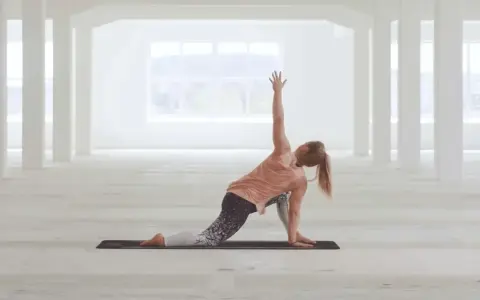 Kvinna utför en vriden yogaställning i ett ljust, öppet rum. Hon fokuserar på sin power yoga-träning.