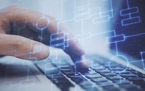 Dłoń na klawiaturze laptopa, nad nią schemat blokowy symbolizujący testy na produkcji.