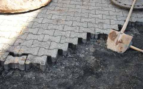 Fragment nawierzchni z kostki brukowej w trakcie układania, obok łopata.