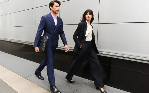 Para idąca w eleganckim business attire, mężczyzna w granatowym garniturze, kobieta w czarnym.