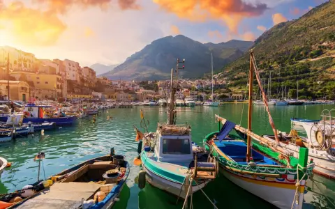 Malowniczy port w Trapani, idealne miejsce na zwiedzanie. Łodzie kołyszą się na wodzie, a w tle widać góry i kolorowe budynki.