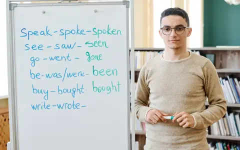 Nauczyciel wyjaśnia formy czasowników, od prostych do tych w **far stopień wyższy i najwyższy**.
