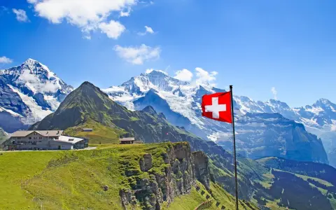 A Swiss flag flies proudly against a backdrop of majestic snow-capped mountains and lush green slopes, showcasing the beautiful places of nature in Switzerland.