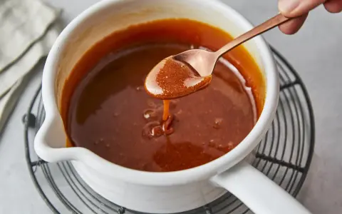 Flüssiges Karamell tropft von einem Löffel in einen Topf. Das Zucker karamellisieren ist fast perfekt.
