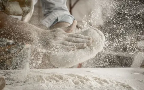 Ręce formują ciasto, a mąka do pizzy unosi się w powietrzu. Idealna do wypieku chrupiącej podstawy.