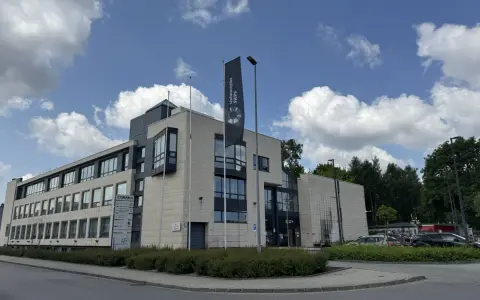 Nowoczesny budynek Uniwersytetu SWPS, jednej z uczelni w Krakowie, z flagą i parkingiem.