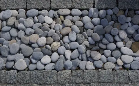 Gładkie, szare kamienie tworzą naturalną dekorację w ogrodzie, otoczone granitową kostką.