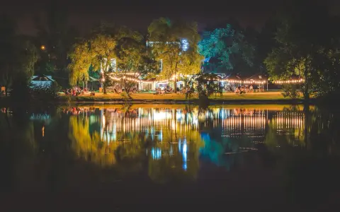Nastrojowa fotografia nocna nad jeziorem, z oświetlonymi drzewami i budynkami, tworzącymi piękne odbicia w wodzie.