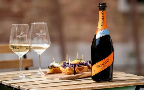 Mionetto alkoholfreier Aperol 0.0% mit zwei Gläsern und leckeren Bruschettas auf einem Holztisch.
