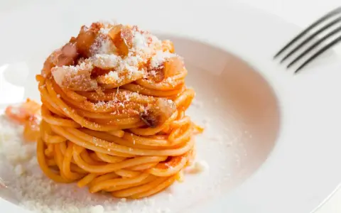 Un piatto di spaghetti alla amatriciana ricetta, conditi con guanciale croccante e pecorino grattugiato, pronti per essere gustati.
