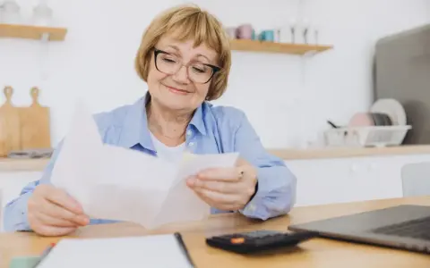 Uśmiechnięta starsza pani z okularami przegląda dokumenty, planując wymianę dowodu osobistego po 70 roku życia.