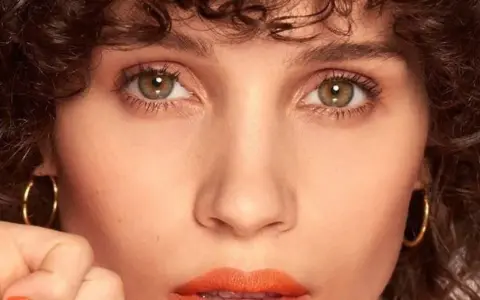 Primer plano de una mujer con rizos oscuros y maquillaje color coral vibrante en los labios.
