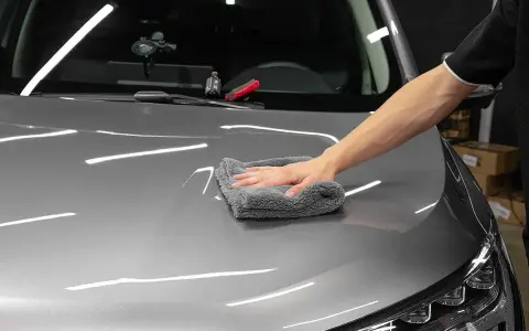 A hand buffs a car's hood with a microfiber cloth, applying a ceramic wax for a deep shine.