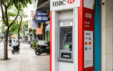 Bankomat HSBC w Hanoi, gotowy do wypłaty waluty. W tle widać ruchliwą ulicę z motocyklami i sklepami.