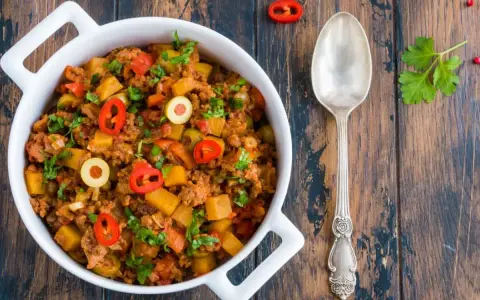 Pyszne danie z mielonego mięsa wołowego z ziemniakami, oliwkami i papryczką chili, posypane natką pietruszki.