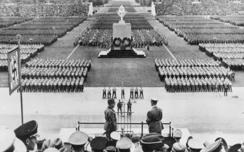 Massenveranstaltung in Nürnberg. Tausende marschieren, Fahnen wehen. Hitler ist anwesend.