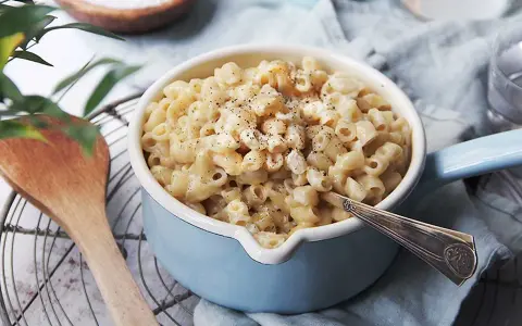 En skål med krämiga stuvade makaroner, toppad med svartpeppar. En träsked ligger bredvid.